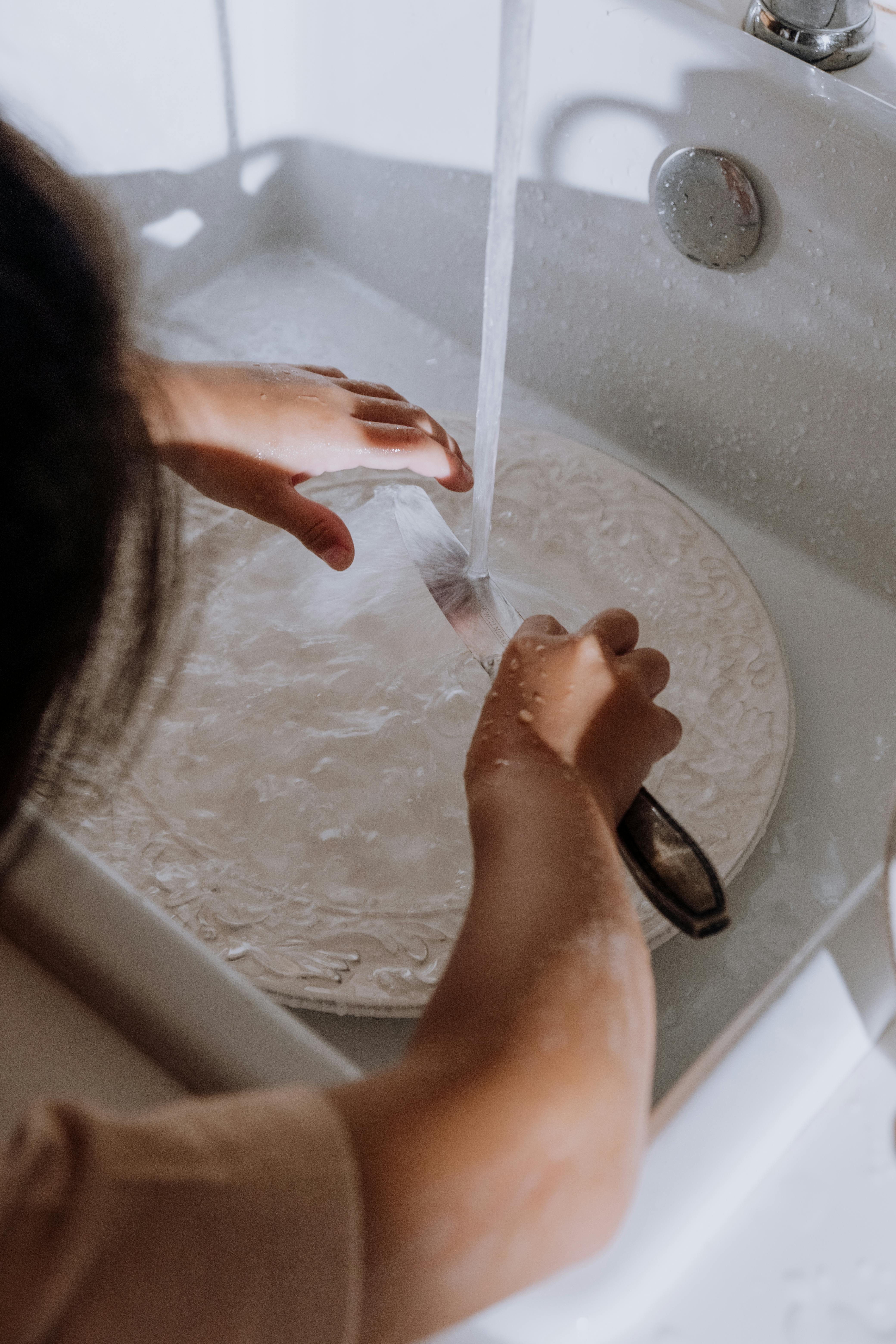 A child carefully washing a plate at the sink.