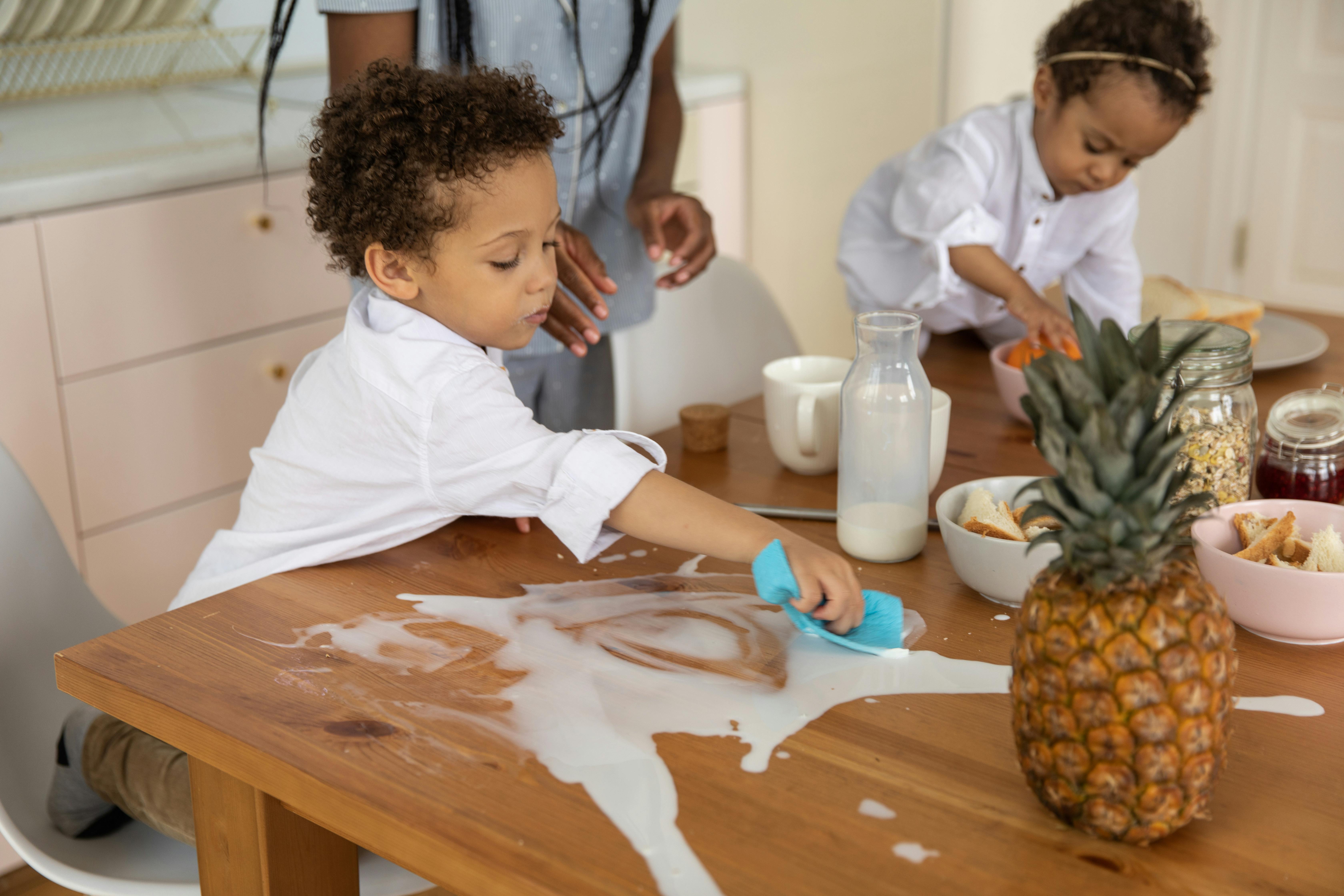 A boy wiping up a breakfast spill at the table.