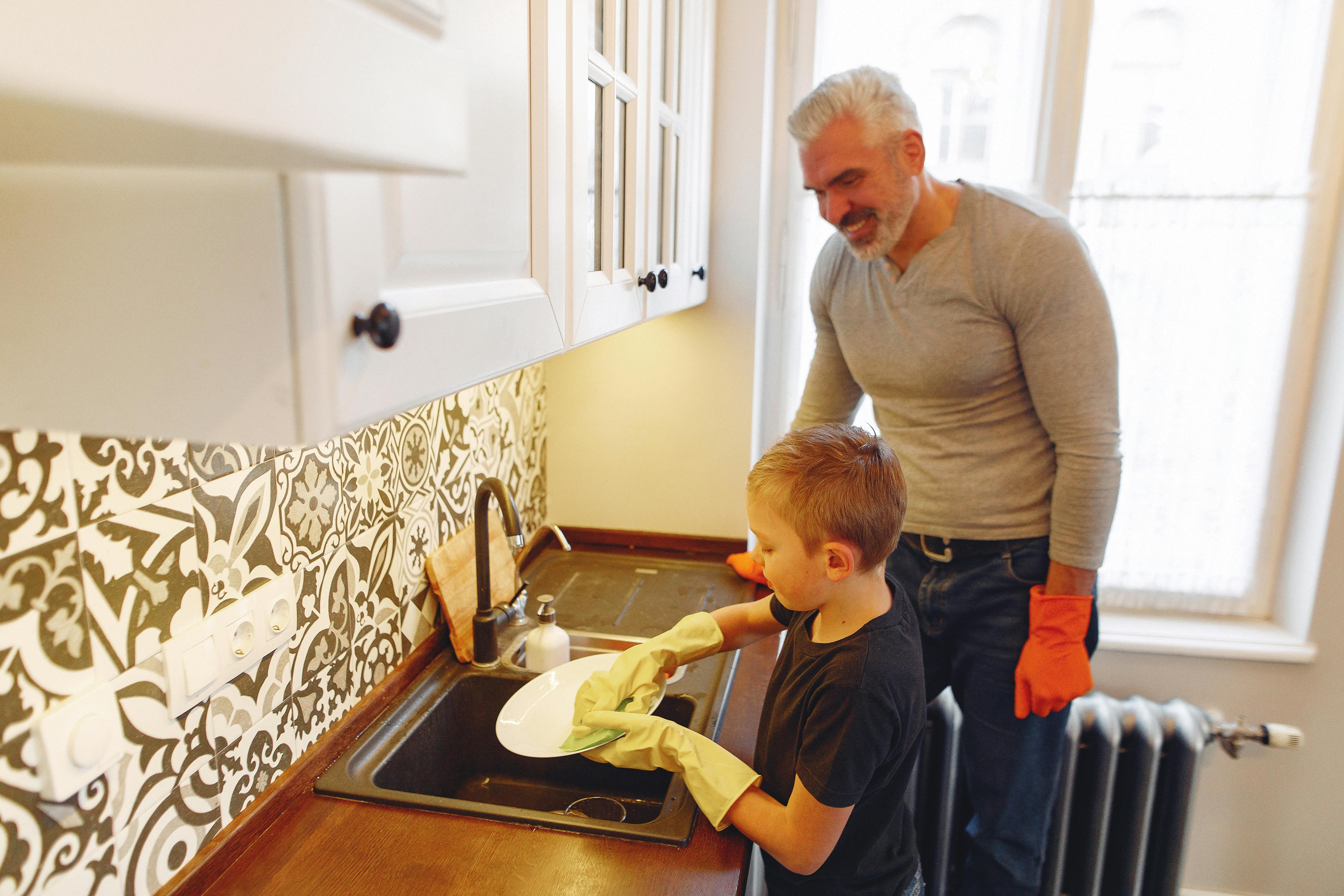 A parent and child washing dishes together at the kitchen sink.